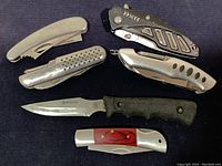 All 6 knives displayed on a dark fabric surface showing different handle styles and profiles, including fixed and folding blades.