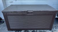 Front view of brown Resin Rubbermaid deck storage box with faux wicker side texture, showing the centered lid handle