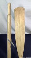 Wooden oar showing handle and blade with attached metal oar lock.