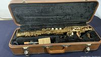 Open case with vintage Monique Pro saxophone inside, showing mouthpiece, ligature, and interior black plush lining.