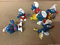 Photo showing six vintage Smurf figurines from the 1980s in various poses and outfits, all molded plastic with painted details.