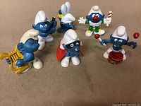 Photo showing 6 vintage 1980s Smurfs figurines with various costumes and accessories, all in used condition.