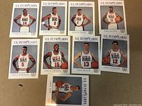 Nine U.S. Olympic basketball trading cards laid out on a flat surface, showing players from the 1990s Dream Team set.