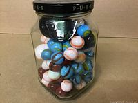 Front view of the glass jar filled with predominantly blue, white, and brown swirled marbles.