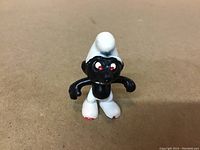 Front-facing photo of a small black Smurf figurine with white hat and pants, showing an angry expression with red eyes and minor wear on the paint of the feet.