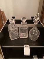 Front view of three crystal decanters showing diamond crosshatch, golfer etching, and teardrop shapes on a black shelf