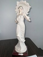 Front full view of Italian Art Deco porcelain figurine of an elegant woman holding an umbrella, on wooden base with artist's plaque.