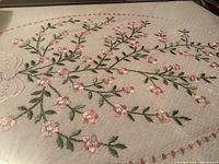Close-up of embroidered coverlet showing pink flowers and green leaves stitched in oval pattern
