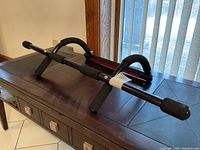 Black metal pull up chin bar placed on a table showing side view with padded handles and mounting grips.
