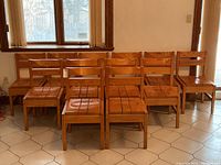 Eight wooden vintage slat-back chairs grouped together in a room, showing the full set as viewed from the front.