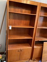 Front view of teak bookcase section showing open shelves and cabinet doors with metal handles.