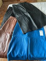 Four vintage leather skirts laid flat, showing different colors: black, brown, electric blue, and black with texture.