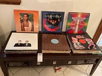 Three stacks of vinyl records on wooden surface, with Whitney Houston, Duran Duran and Earth, Wind & Fire covers displayed upright