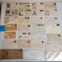 Top-down photo showing a collection of postal covers and envelopes arranged in rows on a white surface with a blue tag labeled '48'. Covers show a variety of stamps and printed addresses, some with propaganda and military themes.