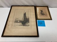 Photo showing two framed nautical sailboat etchings side by side on a white surface with a blue lot number card.