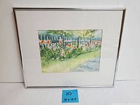 Framed watercolor painting showing white picket fence with flowers, in simple white frame and mat.