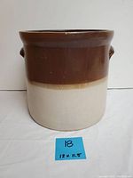 Front view of antique stoneware crock, showing brown upper half and beige lower half with two side handles.