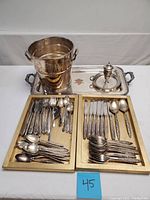 Overview of silverplate ice bucket, serving tray, sugar caster and flatware on wooden trays
