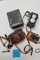 All four vintage cameras arranged flat including Rolleicord, Olympus case, Kodak case, and box camera