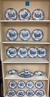 Full view of shelves containing 21 pieces of Johnson Bros Coaching Scenes china including plates, bowls, a platter, and creamer jug. Blue and white with floral and coaching illustrations.