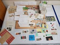 Overview of a large assortment of postage stamps scattered over a table with some arranged on wooden trays, many in envelopes labeled by country.