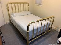 Full view of brass metal bed frame with headboard and footboard in bedroom with mattress and linens on it.