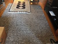 Photo showing the larger textured area rug with the smaller patterned rug laid on top on wooden floor.