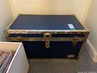 Front angle view of the blue wooden chest with brass metal trim, showing dents on metal edges and lock detail.