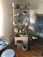 Photo of metal shelving unit holding assorted decorative and serving items including ceramic, wicker, and glass pieces