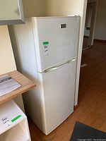 White Frigidaire refrigerator with top freezer shown from side angle, showing scale and location next to kitchen counter.