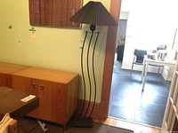 Floor lamp standing next to a wooden cabinet with a green wall background, showing full height and base.