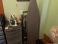 Photo showing ironing board, metal clothes rack, plastic storage drawers, and Osrow Steamstress iron on top