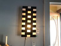 Front view of the rectangular wall-mounted light fixture with checkerboard pattern, illuminated showing alternating black and translucent squares.
