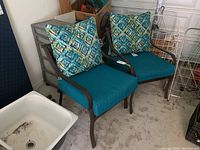 Two patio chairs indoors with dark metal frames, teal seat cushions, and blue-green-yellow patterned back cushions.