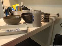 Overview photo showing the tray, two pottery bowls, ceramic mug with HB logo, and boat-shaped container on a white surface