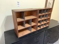 Two wooden shelving units side by side on a black surface against a wall, showing compartments and hinges.