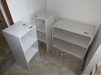 Three white MDF shelving units positioned in a corner, two tall narrow units and one wider low unit, all showing wear and dirt.