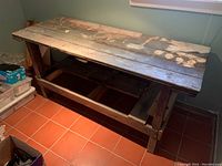 Side view showing the work bench's wood structure, thick planks, signs of damage and wear, and open lower frame.