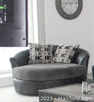 Front view of round swivel loveseat with black faux leather and grey fabric seat cushion, includes two patterned accent pillows