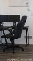 Side view of black office chair in front of L shaped office desk. Shows desk frame and floor area.