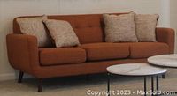 Front view of orange mid-century modern sofa with four matching patterned throw pillows