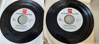 Two black 45 RPM vinyl records with white center labels and red Coca Cola logo, both in original paper sleeves.