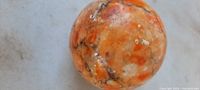 Top view of the marble ball showing the mixed orange, tan, and cream coloration with natural black veins.