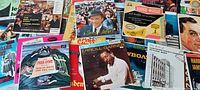 Photo showing an assortment of approximately 45 RPM vintage records laid out, revealing colorful cardboard sleeves with various artists and titles such as Erroll Garner, Bobby Sherwood, Harry James, and more.