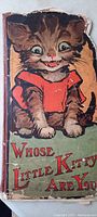 Front cover of the children's story book featuring a large illustration of a kitten wearing a red shirt. The cover is shaped to follow the outline of the kitten and shows wear and creases around edges.