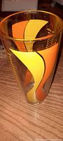 Photo showing tall glass measuring cup with orange and yellow decorative swirls on clear heavy glass.