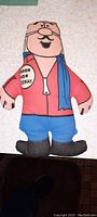 Full view of the vintage plush advertising doll Baron Von Esskay from Esskay Meats, showing front with red shirt, blue scarf, blue pants, black boots and the printed badge on left arm.