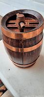 Front view of a small vintage wooden barrel with dark metal bands and wooden spigot on top, showing intact construction and overall condition.