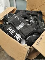Open cardboard box filled with folded dark gray Meteor brand T-shirts