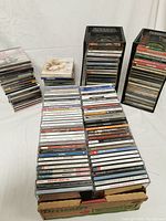 Multiple stacks of approximately 100 music CDs in jewel cases, photographed to show the range and quantity.
